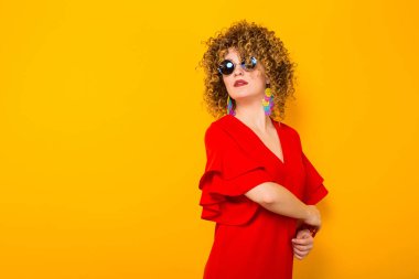Çekici genç kıvırcık saçlı kadın kırmızı elbise ve poz güneş gözlüğü