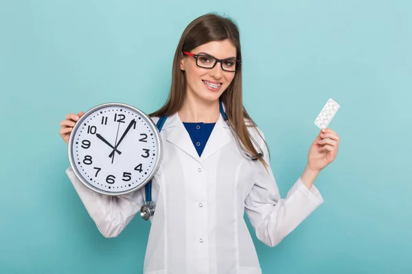 自信的年轻女性医生用听诊器持有药丸和时钟 — 图库照片