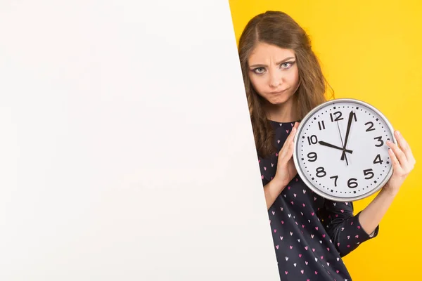 stock image Pretty brunette girl with blank billboard holding clock and looking at camera