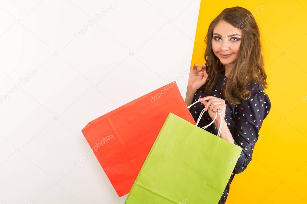 Pretty brunette girl with blank billboard holding shopping bags