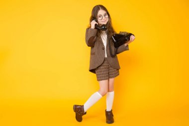 Cute little brunette girl talking on old telephone on yellow background  clipart