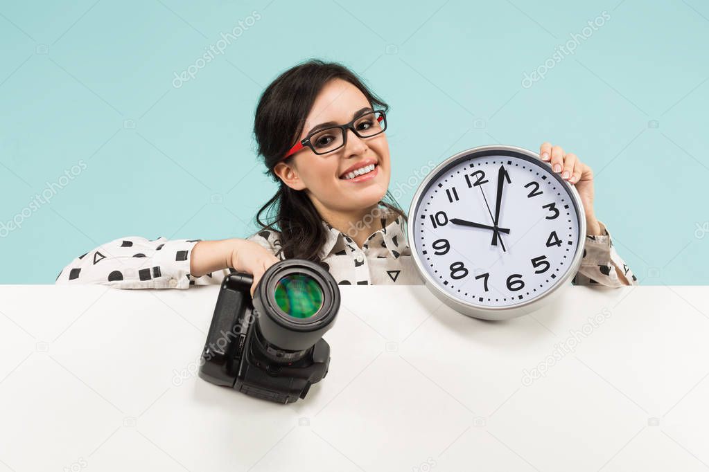 Young brunette woman holding professional photo camera and wall clock