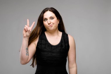 Studio gri duvar farklı ifadeler gösterilen basit siyah gömlekli uzun lüks saçlı güzel curvy esmer kadın.