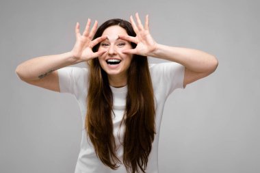 Studio gri duvar farklı ifadeler gösterilen basit beyaz t-shirt uzun lüks saçlı güzel curvy esmer kadın.