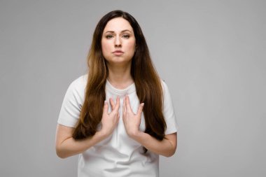 Studio gri duvar farklı ifadeler gösterilen basit beyaz t-shirt uzun lüks saçlı güzel curvy esmer kadın.