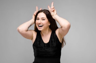 Studio gri duvar farklı ifadeler gösterilen basit siyah gömlekli uzun lüks saçlı güzel curvy esmer kadın.