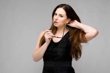 Studio gri duvar farklı ifadeler gösterilen basit siyah gömlekli uzun lüks saçlı güzel curvy esmer kadın.