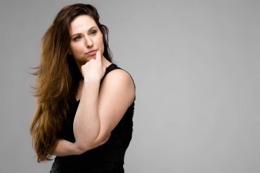 Studio gri duvar farklı ifadeler gösterilen basit siyah gömlekli uzun lüks saçlı güzel curvy esmer kadın.