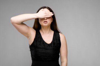 Studio gri duvar farklı ifadeler gösterilen basit siyah gömlekli uzun lüks saçlı güzel curvy esmer kadın. El kapalı gözleriyle.