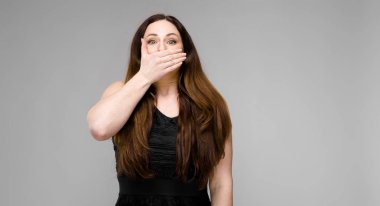 Studio gri duvar farklı ifadeler gösterilen basit siyah gömlekli uzun lüks saçlı güzel curvy esmer kadın. El ağzı kapatma.