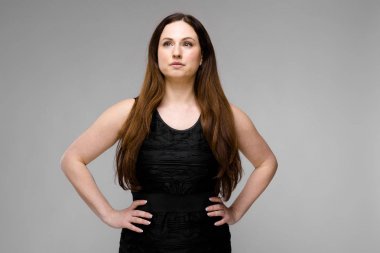 Studio gri duvar farklı ifadeler gösterilen basit siyah gömlekli uzun lüks saçlı güzel curvy esmer kadın.