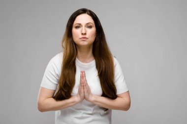 Studio gri duvar farklı ifadeler gösterilen basit beyaz t-shirt uzun lüks saçlı güzel curvy esmer kadın.