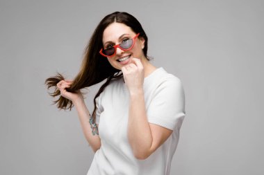 Studio gri duvar farklı ifadeler gösterilen basit beyaz t-shirt uzun lüks saçlı güzel curvy esmer kadın.