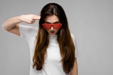 Basit beyaz t-shirt ve gri duvar Studio farklı ifadeler gösterilen kırmızı plastik parti güneş gözlüğü uzun lüks saçlı güzel curvy esmer kadın.