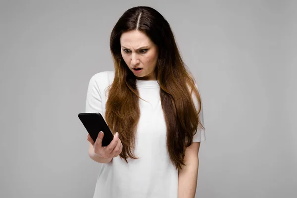 携帯電話で話しながら灰色の壁にさまざまな表現を示すシンプルな白い シャツで髪の長い豪華な美しい曲線のブルネットの女性 — ストック写真