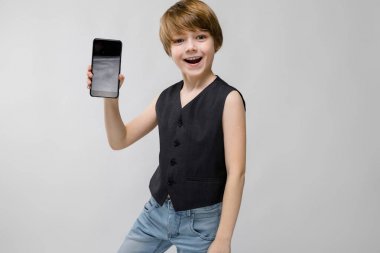 Sevimli beyaz çocuk farklı ifadeler gösterilen ve beyaz duvar Studio smartphone dolar yığını ile tutarak siyah kıyafeti.