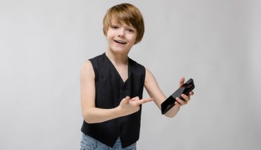 Sevimli beyaz çocuk farklı ifadeler gösterilen ve smartphone Studio beyaz duvar üzerinde tutarak siyah kıyafeti.
