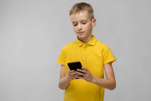 可爱的金发白人青春期男孩在明亮的 T恤显示不同的表现在白色的墙壁在演播室 看智能手机屏幕 — 图库照片