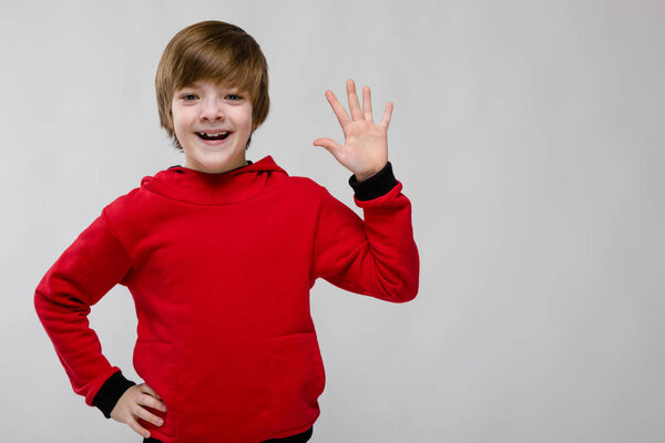Nice preteen caucasian boy in casual outfit showing different expressions on white wall in studio. Smiling and waving hand.