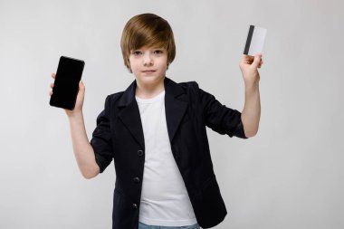 İyi preteen beyaz çocuk farklı ifadeler gösterilen ve beyaz duvar Studio smartphone ile kredi kartı tutan gündelik kıyafeti.