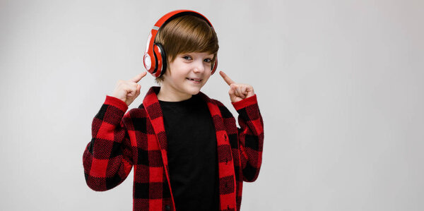 Милый юный кавказский мальчик в повседневной одежде слушает музыку в красных наушниках и показывает различные выражения на белой стене в студии
.