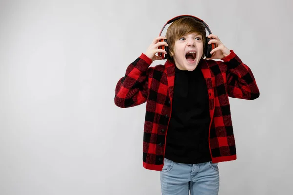 尼斯青春期白种男孩在休闲装听音乐在红色耳机和显示不同的表现在白色墙壁在演播室 — 图库照片