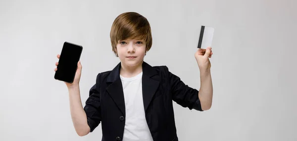 尼斯青春期白种男孩在休闲装显示不同的表达式和手持智能手机与信用卡在演播室白墙 — 图库照片