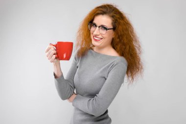 Güzel kıvırcık saçlı Kafkas kadın gözlük ve gri elbise beyaz duvar Studio farklı duygusal ifadeler gösteriliyor. Fincan kahve ile gülümseyen.