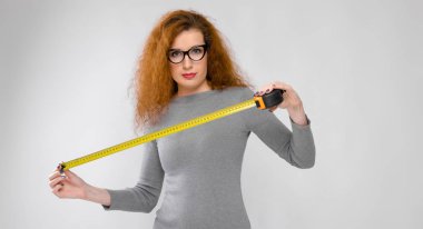 Güzel kıvırcık saçlı Kafkas kadın gözlük ve gri elbise beyaz duvar Studio farklı duygusal ifadeler gösteriliyor. Ölçülür şerit germe.