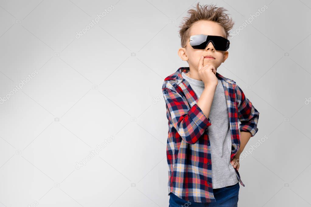 Nice caucasian preschooler boy in casual outfit and sunglasses showing different expressions on white wall in studio.