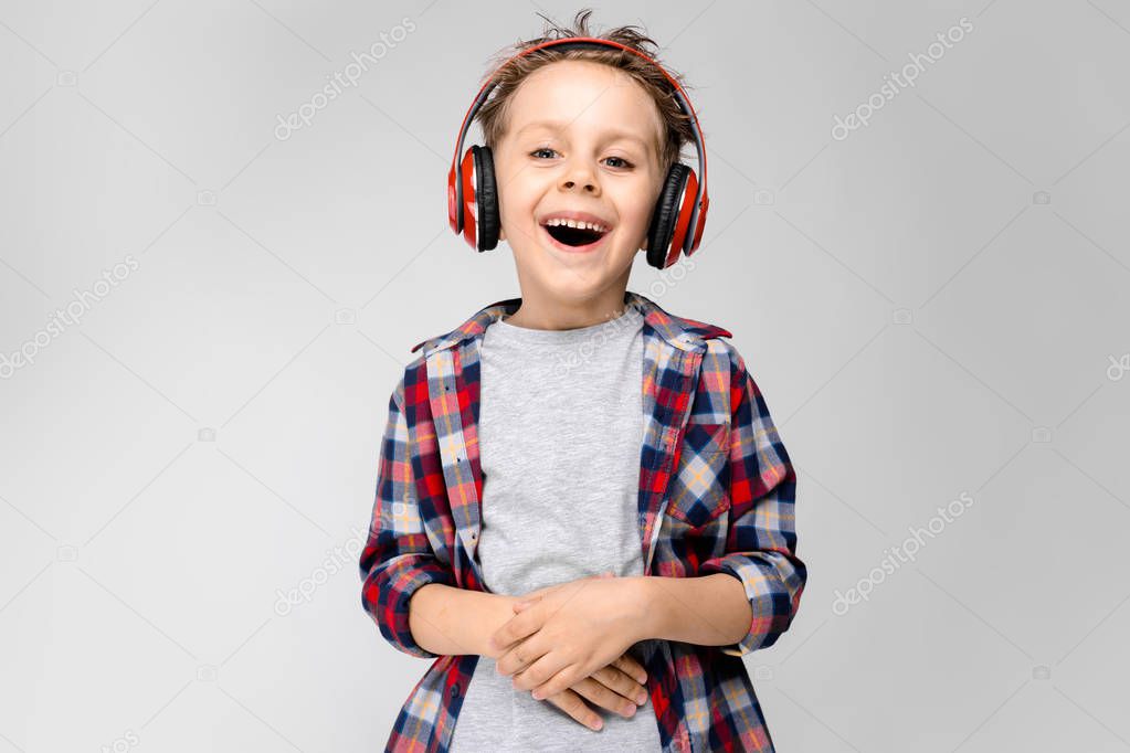 Nice caucasian preschooler boy in casual outfit posing with red headphones and showing different expressions on white wall in studio.