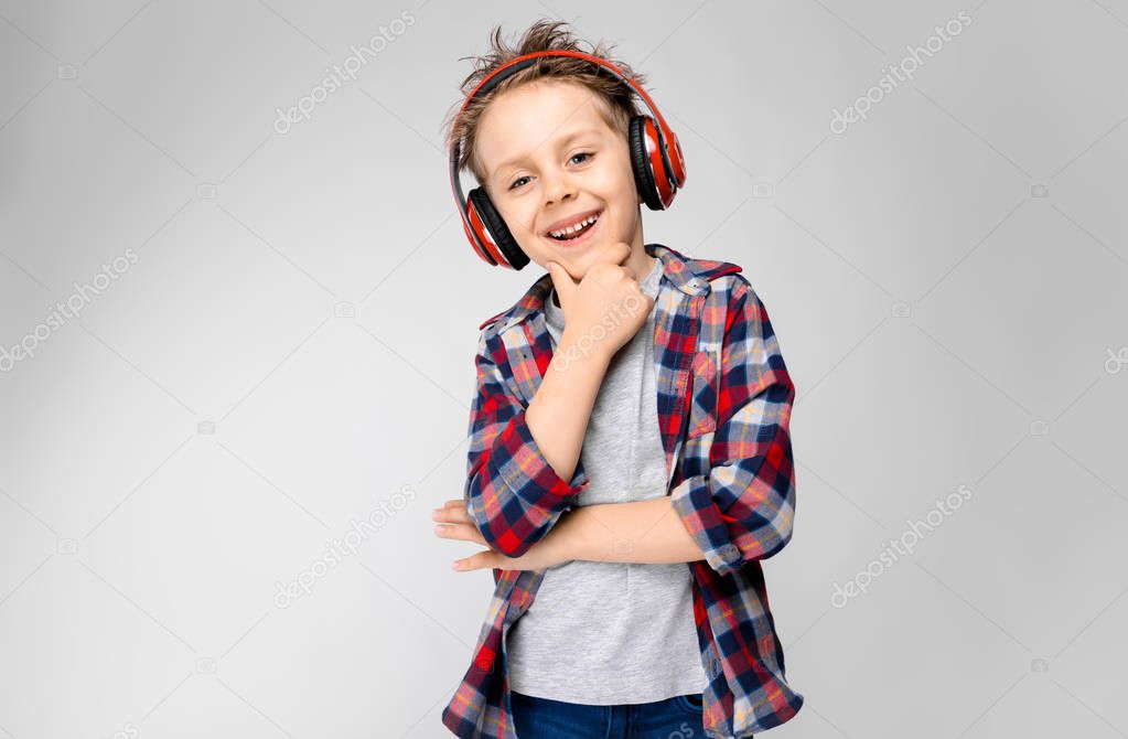 Nice caucasian preschooler boy in casual outfit posing with red headphones and showing different expressions on white wall in studio.