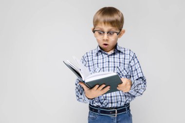 Çok güzel ciddi emin küçük çocuk gri arka plan üzerinde kitap okuma bardaklarda portresi