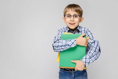 Gri arka plan üzerinde renkli klasörler tutan gözlüklü şirin küçük çocuk portresi