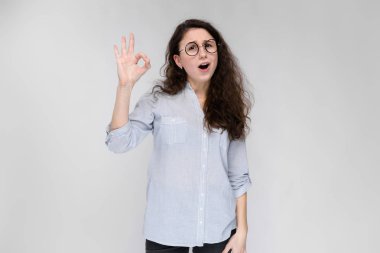 Çekici genç kıvırcık esmer beyaz kadın ok işaret gri izole gösteren gözlük