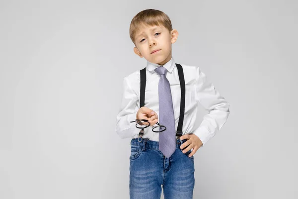 灰色の背景にサスペンダーのズボンを着てかわいい深刻な自信を持っている小さな男の子の肖像画 — ストック写真