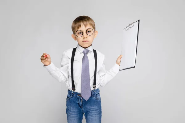 灰色の背景にクリップボードを保持しているメガネで愛らしい深刻な自信を持って小さな男の子の肖像画 — ストック写真