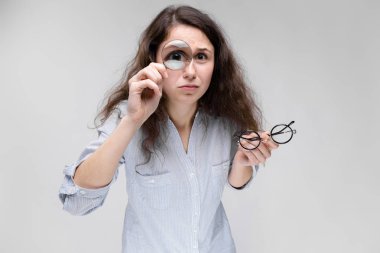 Gözlük ve gri izole Büyüteç işaret tutan çekici genç kıvırcık esmer beyaz kadın