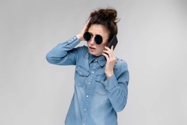 Genç esmer beyaz kız topuz saç modeli gri izole smartphone kullanarak güneş gözlüğü ile