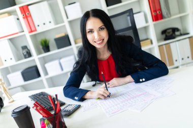 Güzel genç kız ofiste belgelerle masada çalışıyor ve bir kalem elinde tutuyor.