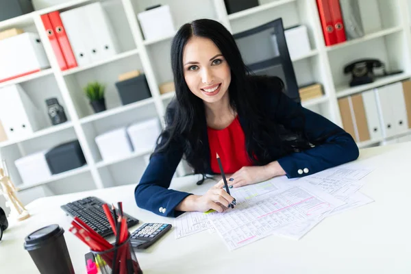 Güzel genç kız ofiste belgelerle masada çalışıyor ve bir kalem elinde tutuyor.