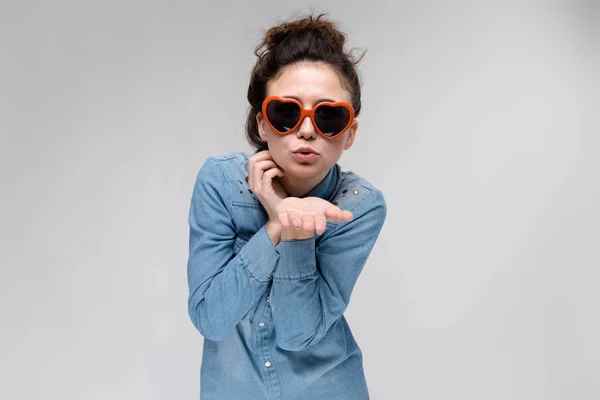 Junges brünettes Mädchen mit Brille in Form eines Herzens. Die Haare sind zu einem Dutt zusammengebunden. das Mädchen schickt einen Luftkuss. — Stockfoto