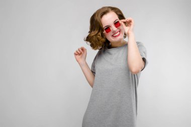 Gri T-shirt gri bir arka plan üzerine sevimli genç kız. Kırmızı kare gözlü gözlüklü kız.