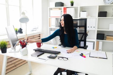 Genç bir kız ofiste bir masada oturur ve bir kalem vazolar ağaç.