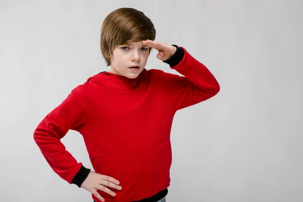 Lindo niño caucásico confiado en suéter rojo mirando a la distancia sobre fondo gris —  Fotos de Stock