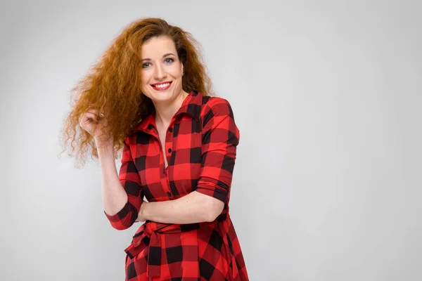 Jonge roodharige meisje in een rode geruite shirt. Jong meisje heeft haar haren met haar hand — Stockfoto