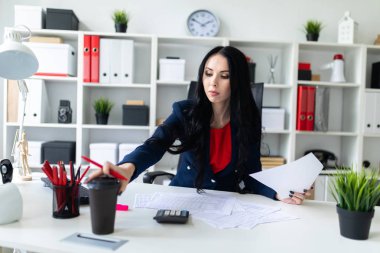 Güzel genç kız masa ofis belgeleri ile çalışıyor. Kız bir bardak kahve ile masaya yatıyor.