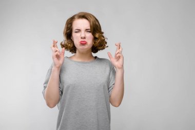 Gri T-shirt gri bir arka plan üzerine sevimli genç kız. Kız onun kollarında onun parmak çarpı işareti