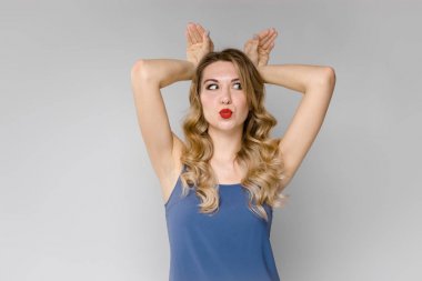 Güzel bir genç kızın kafasına iki el koyarak ve yüzünü büküm aptallar. Gri bir arka plan üzerine bir genç kızın komik portre