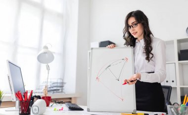 Güzel bir genç kız bir Ofis Masası standları ve manyetik bir işaretleyici manyetik tahtaya çizer.